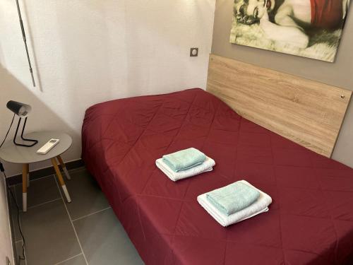 - un lit rouge avec 2 serviettes dans une chambre dans l'établissement GOLFE JUAN Joli F2 clim piscine à 5 minutes de la mer, à Vallauris