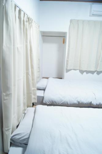 two beds in a room with white curtains at ゲストハウスはれのち in Furunoushigawa