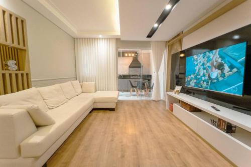 a living room with a white couch and a flat screen tv at Belíssimo Apartamento MJ44 in Maringá