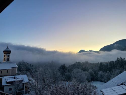 a misty valley with a building and a church with a clock tower at Rosa Alpina Appartement in Bürserberg
