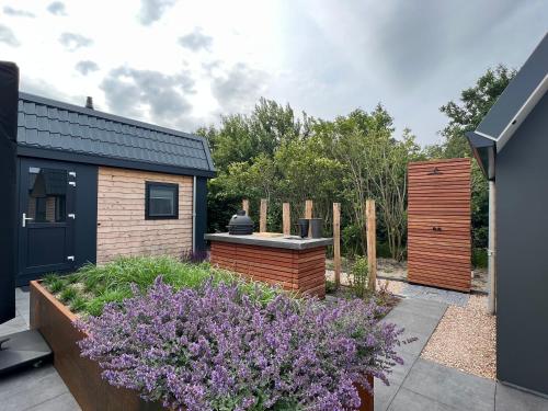 a garden with purple flowers in front of a house at Qué Vida, Boutique Chalet aan Zee en Meer in Scharendijke