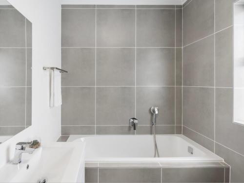 バリートにあるSpacious Ballito Village Apartmentのグレータイルのバスルーム(白いバスタブ付)