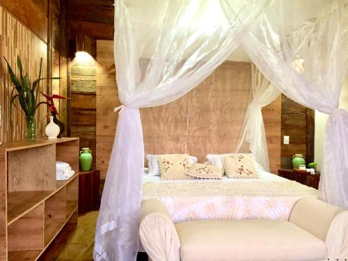 a bedroom with a white canopy bed with a couch at Bangalô Maria Vista Mar, Luxo em Trancoso in Porto Seguro