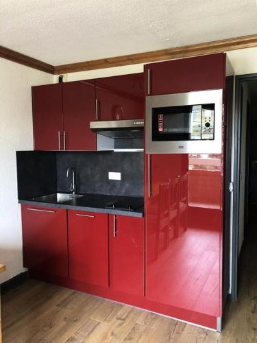 - une cuisine rouge avec évier et four micro-ondes dans l'établissement Résidence Bergers P&v - APPARTEMENT ALPE D'HUEZ QUARTIER BERGERS MAE-2371, à Huez