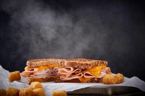 a sandwich with meat and cheese on a plate with tater tots at Drury Plaza Hotel Dallas Richardson in Richardson