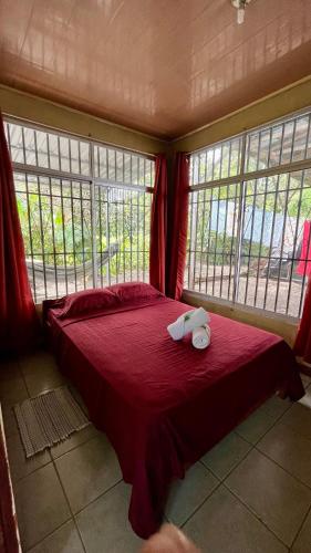 a bedroom with a bed with red sheets and windows at Blue House with Air-Conditioning in Puerto Jiménez