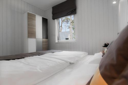 a bedroom with a bed with white sheets and a window at Wakacyjne Domki in Pogorzelica