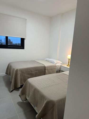 Dos camas en una habitación blanca con ventana. en ETOCS - Departamento con piscina - Excelente ubicación - Opcional cochera, en Bahía Blanca