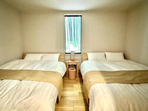two twin beds in a room with a window at and FOREST勝浦 竹の離れ 美しい竹林に囲まれ露天風呂とSAUNAを楽しむ大人の離れ 天然鉱泉 BBQ ペット 最大8名 勝浦 in Katsuura
