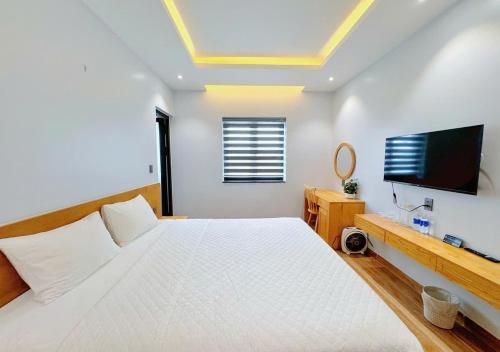 a white bedroom with a large bed and a flat screen tv at Bay Homestay in Cam Lâm