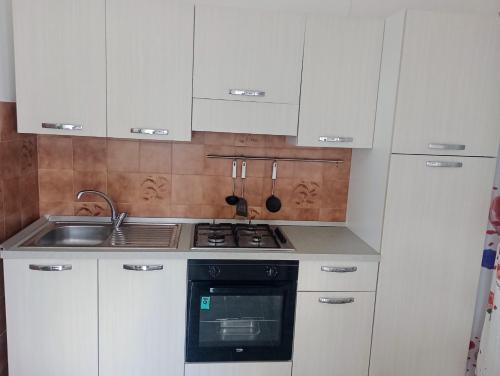 a kitchen with white cabinets and a stove and a sink at PignaRossa Appartamenti in Mongiove