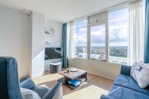 a living room with a blue couch and a large window at Appartementencomplex Juliana 128 in De Koog