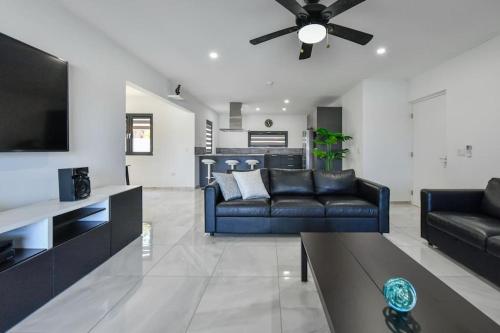 a living room with two black leather couches and a tv at New Villa Luel 5 minutes from Palm Beach in Noord