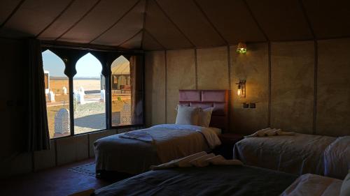 a bedroom with two beds and a large window at La Sultana Luxury Camp in Merzouga