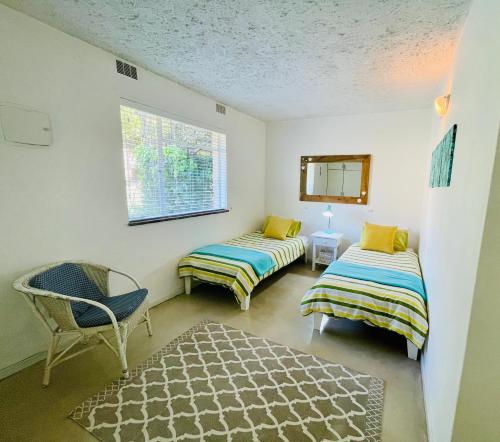 a room with two beds and a chair and a window at Panorama Sea-View Apartment in Plettenberg Bay