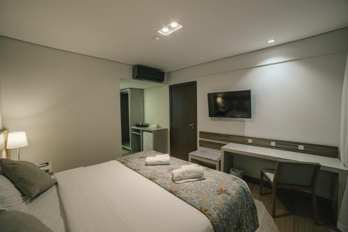 a bedroom with a bed and a desk and a television at Interludium Iguassu Convention Hotel in Foz do Iguaçu