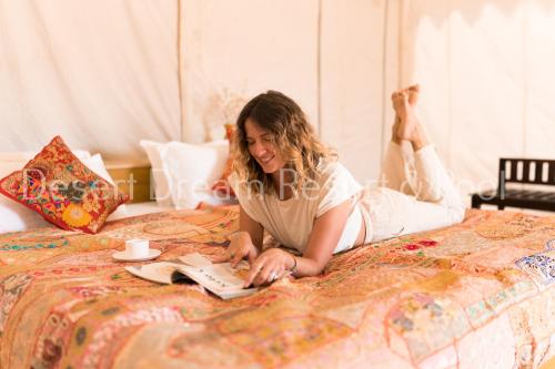 a woman laying on a bed reading a book at Desert Dream Royal Camp & Pool in Jaisalmer