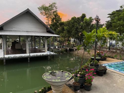 a house and a pond with a table and flowers at Cozy breezing countryside Pet in Ban Khlong Sip Sam Lang