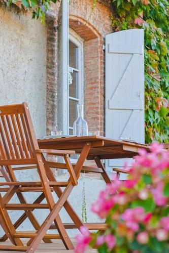 a wooden table and chair on a patio with pink flowers at La Maison des Champs in Cintegabelle