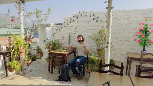 a man sitting at a table in a room with plants at Hotel White House - A Family Homestay in Pushkar
