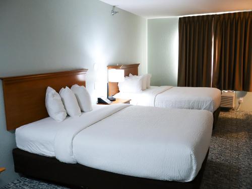 two beds in a hotel room with white pillows at Travelodge by Wyndham Rapid City - Black Hills in Rapid City