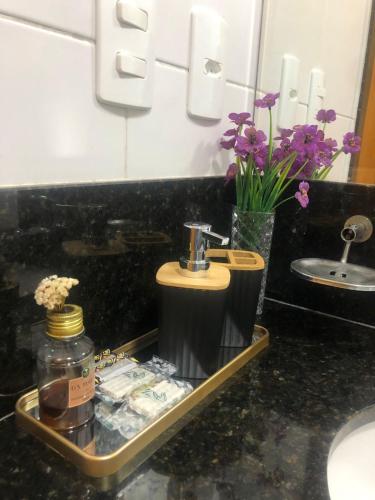 a bathroom sink with a soap dispenser and flowers at Flat Lux - com Piscina e Netflix in Rio de Janeiro