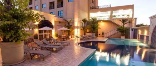 a hotel with a pool and chairs and a building at Flat Araucaria Plaza in Ribeirão Preto