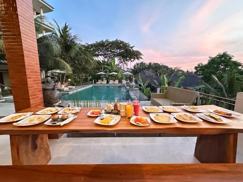 a wooden table with plates of food on it next to a pool at Brata Cottage Ubud in Ubud