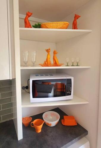 a kitchen shelf with a microwave and bowls and glasses at Rosebud Retro Retreat in Rosebud