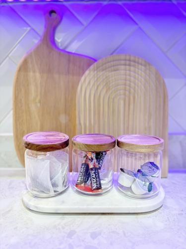 three glass jars on a plate with a wooden table at Lux Stays - Luxury Leeds City Apartment with Jacuzzi & Free Parking in Leeds