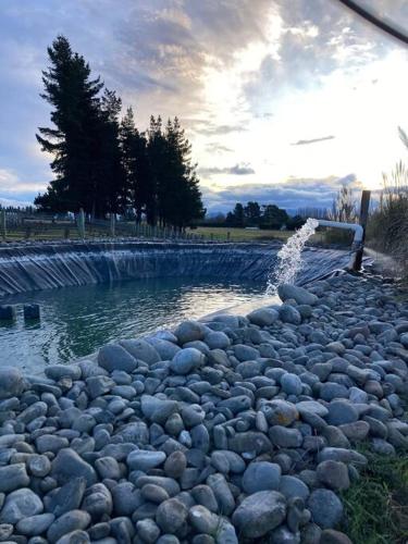 a stream of water with rocks in front of a fountain at Kingfisher cottage in Hurunui