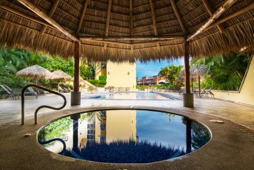 a pool at a resort with a straw roof at Apartotel & Suites Villas del Rio in San José