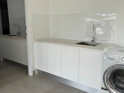 a white kitchen with a sink and a washing machine at Family size tropical oasis retreat netflix wifi in Redlynch
