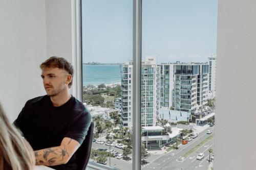 a man standing in front of a window looking at the ocean at Aquavista Penthouse - Stunning 180 Views in Maroochydore