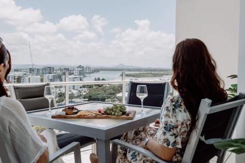 two people sitting at a table with a plate of food and wine at Aquavista Penthouse - Stunning 180 Views in Maroochydore