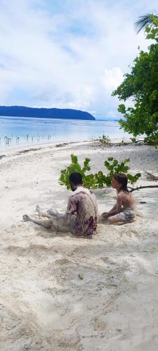 two people sitting in the sand on a beach at Indos Homestay-Raja Ampat in Besir