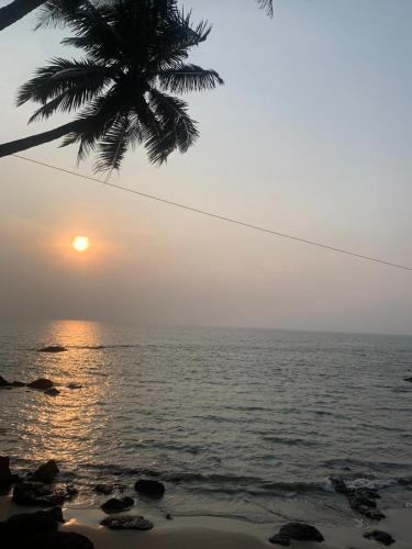 a sunset over the ocean with a palm tree at Om Ganesh Guest House Cliffside in Arambol