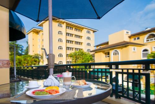 a table with plates of food on a balcony with an umbrella at Apartotel & Suites Villas del Rio in San José
