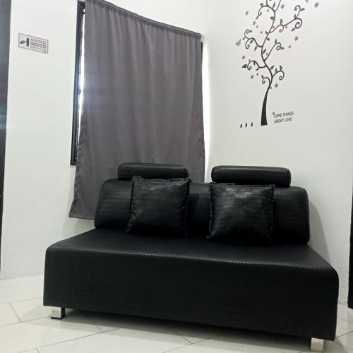 a black couch in a room with a tree on the wall at The 88 Homestay in Batu Pahat