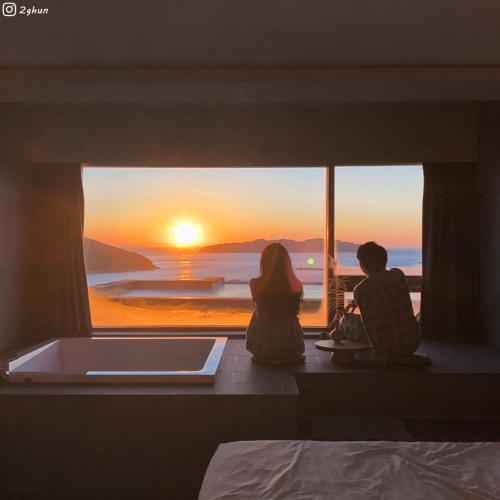 two people sitting on a window sill watching the sunset at Hotel SANG SANG & Private SANG SANG POOL VILLA in Geoje 