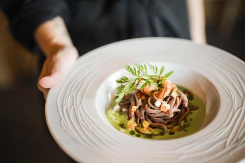 a person holding a white plate with a bowl of food at Boutique Pension Erlacher - Adults Only in Villandro