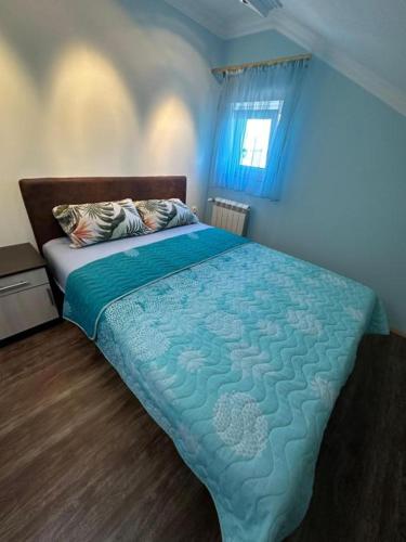 a bedroom with a bed with a blue comforter and a window at Adel's in Subotica