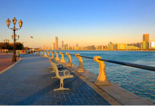 a row of benches on a sidewalk next to the water at Bright Stay Abu Dhabi in Abu Dhabi