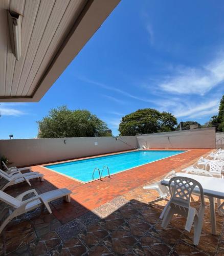 a swimming pool with white chairs and a table at Tulipa Hotel in Foz do Iguaçu