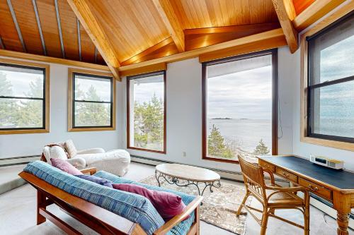 a living room with a couch and a table and windows at Oceanfront Gem in East Boothbay