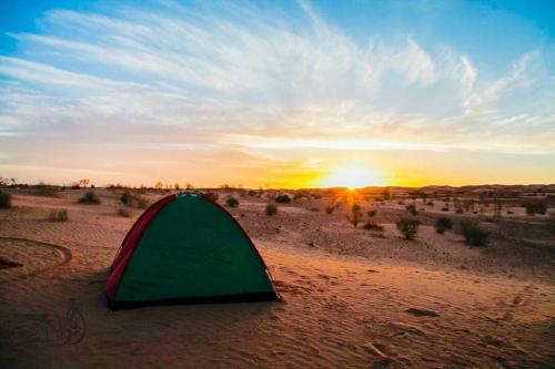 a green tent in the desert with the sunset at Desert Heart in Bidiyah