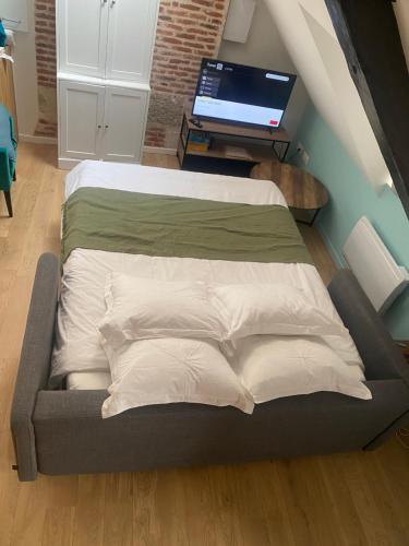 Cette chambre comprend un lit avec des oreillers blancs et une télévision. dans l'établissement LE PAPILLON BLEU, à Honfleur