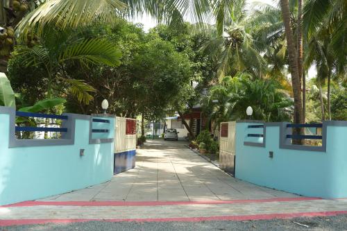 a gate to a driveway with palm trees at Tropical Island Homestay in Payyannūr