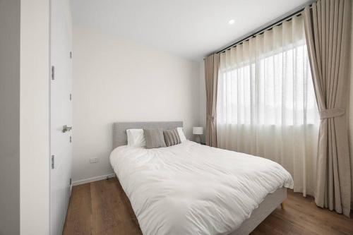 a white bedroom with a bed and a window at Greenstead Retreat 11 beds, 8 bedrooms, 5 baths in Auckland