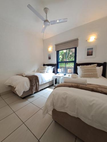 a white bedroom with two beds and a window at Easy Breezy at 18 Thira Santorini in Ballito
